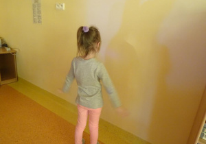 Dziewczynka stoi pod ścianą, obserwuje cień.